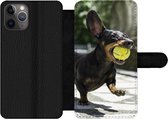 Bookcase Geschikt voor iPhone 11 Pro Max telefoonhoesje - Een zwarte Teckel met een tennisbal - Met vakjes - Wallet case met magneetsluiting