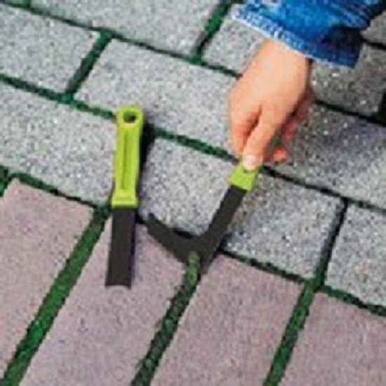 Een hand veegt onkruid uit voegen met een gebogen schraper met groen handvat.