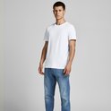 Man in een wit T-shirt en blauwe spijkerbroek, staand, licht gedraaid.