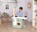 Een jongen in een blauw shirt speelt met een mintgroene speelkeuken met een witte wasbak, kookplaat en oven.