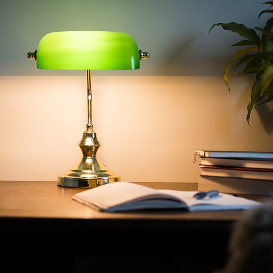 Lampe de bureau verte avec base et bras dorés, à côté d'un livre ouvert sur un bureau.