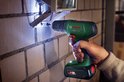 Hand boort met groene Bosch accuboormachine in muur. LED-lampje verlicht het werkgebied.