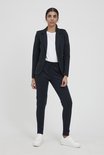 Een vrouw met donker haar draagt een marineblauwe blazer en bijpassende broek met touwtjes. Ze draagt een witte t-shirt en witte sneakers.