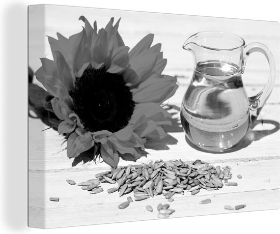 Canvas Schilderij Zonnebloempitten met zonnebloemolie in een klein glas en zonnebloem op witte tafel - zwart wit - 90x60 cm - Wanddecoratie