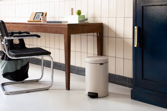 Crème Brabantia NewIcon pedaalemmer naast een houten bureau met een stoel.