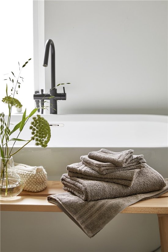 Pile de serviettes taupe sur une étagère en bois à côté d'un vase à fleurs.
