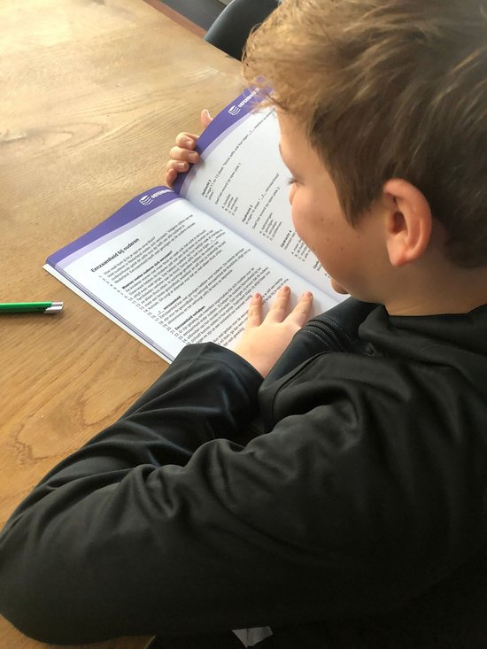 Een jongen met een zwart vest leest een boek. De pagina's zijn gevuld met tekst.