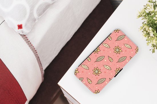 Telefoonhoesje met roze print van gele bloemen en bruine blaadjes, liggend op een nachtkastje naast een bed.
