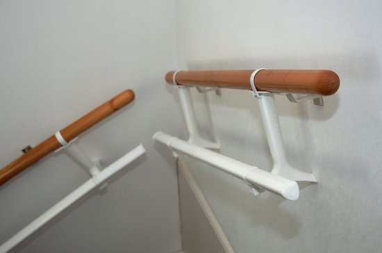 Twee houten trapleuningen met witte beugels, een gebogen, een recht.