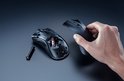 Een hand plaatst batterijen in de onderkant van een zwarte draadloze gamingmuis, met een extra batterij ernaast.