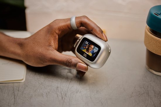 Hand met ring houdt blauwe JBL charging case met display vast.