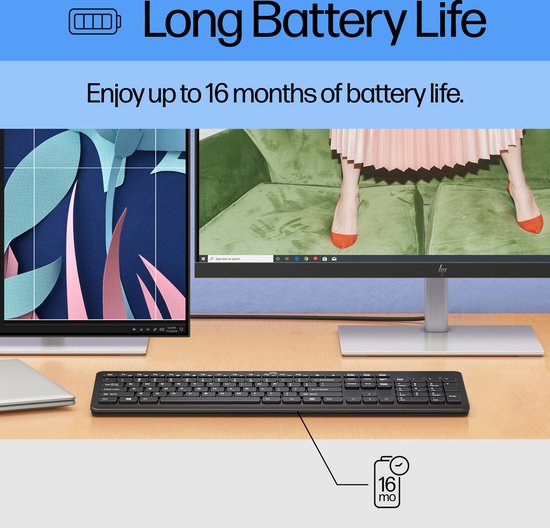 Zwart HP toetsenbord op een bureau, met twee monitoren die een creatieve werkplek tonen. Batterijduur tot 16 maanden.