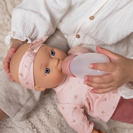 Een pop met roze outfit wordt gevoed met een flesje door een meisje.