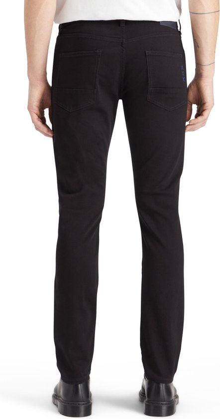 Zwarte jeans gedragen door een man, achterkant zichtbaar. Donkerblauw logo op de rechter achterzak.