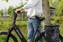 Zwarte Sparta e-bike met een man in spijkerbroek en witte hoodie, met zwarte zadeltas.