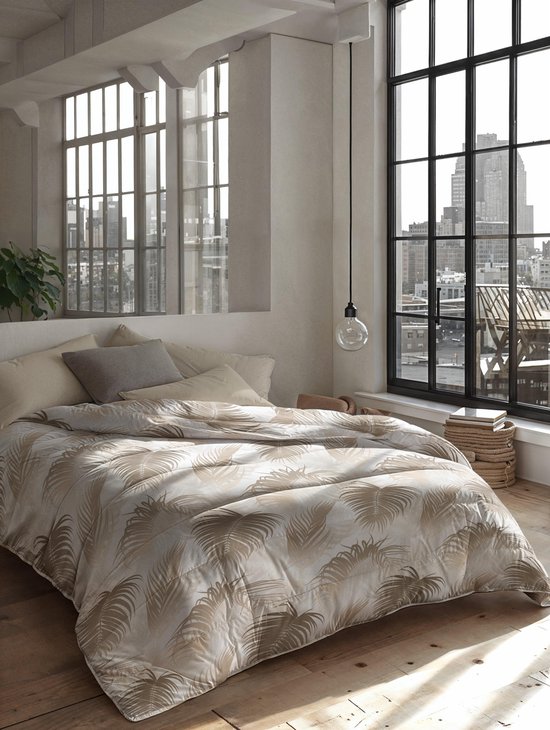 Een gedecoreerd bed met een dekbed met palmbladeren in een slaapkamer met grote ramen.