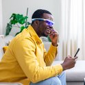 Man met blauwe lichtbril lacht terwijl hij een telefoon vasthoudt.