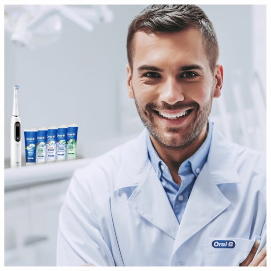 Man in witte doktersjas lacht, met Oral-B elektrische tandenborstel en tandpastabuisjes op achtergrond.