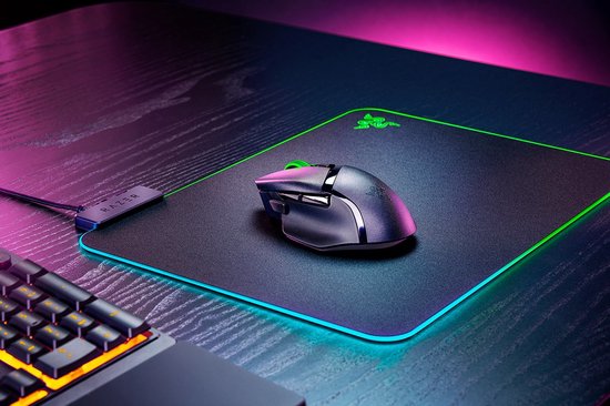 Zwarte Razer Basilisk V3 X Hyperspeed muis met groen scrollwheel op zwarte muismat met gloeiende rand.