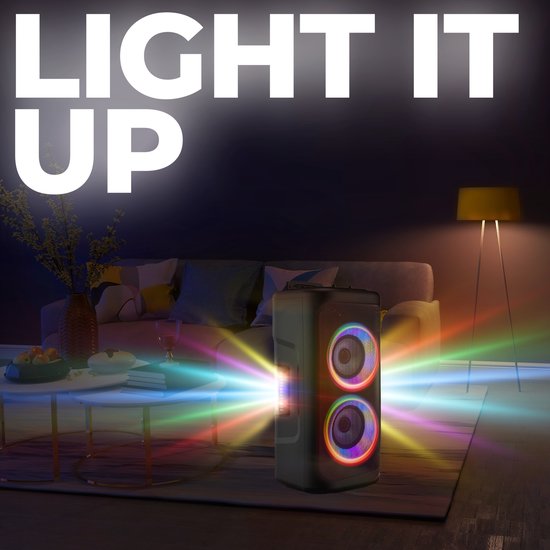 Zwarte party speaker met dubbele woofers en gekleurde lichten, in een woonkamer met sfeerverlichting.