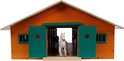 Houten paardenstal met oranje bakstenen façade, grote groene dubbele deuren, witte paard in deuropening.