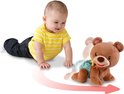 Baby in geel-wit gestreept shirt en spijkerbroek kruipt achter een bewegende bruine beer aan.