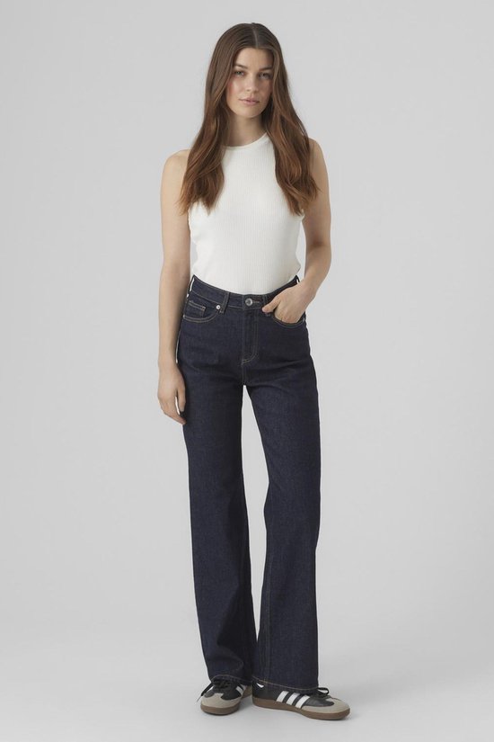 Model met donkerblauwe spijkerbroek met wijde pijpen en hoge taille, gedragen met wit topje.