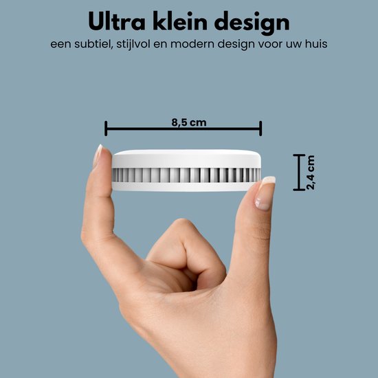 Hand houdt kleine, witte, ronde rookmelder vast. Afmetingen 8,5 cm breed en 2,4 cm hoog. Tekst: Ultra klein design.