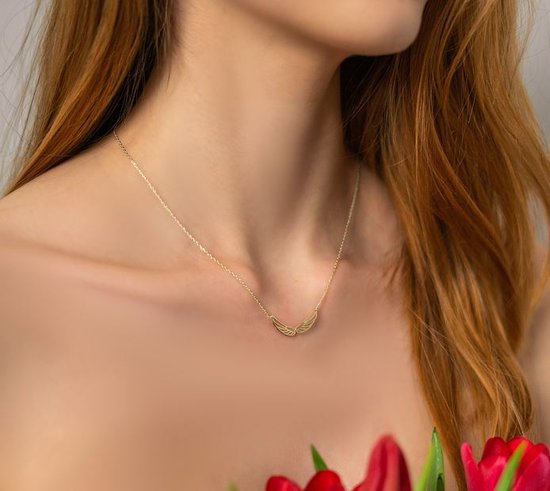 Gouden ketting met vleugelvormige hanger op de hals van een model.