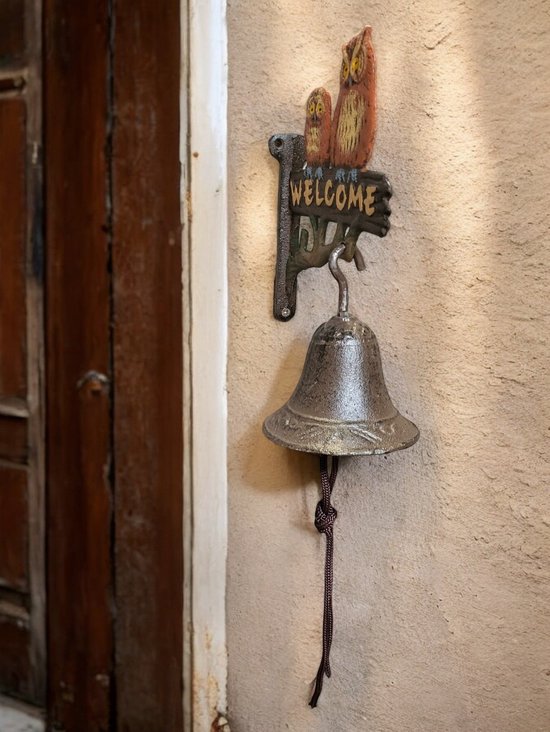 Gietijzeren deurbel met twee bruine uilen en 'WELCOME' bord, naast een houten deur.