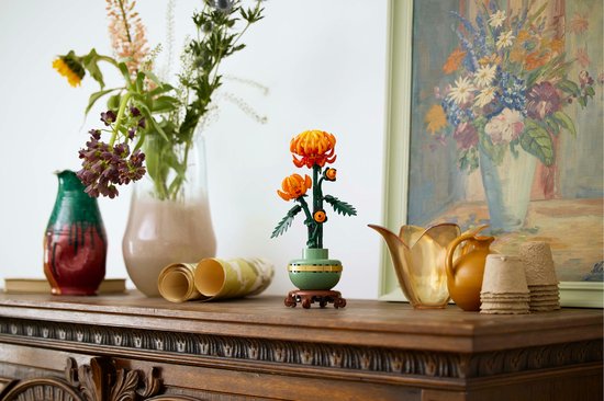 Chrysanthème LEGO dans un pot vert pastel sur socle en bois, sur meuble en bois avec vases.