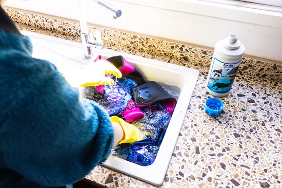 Wetsuit wassen in spoelbak met gele handschoenen