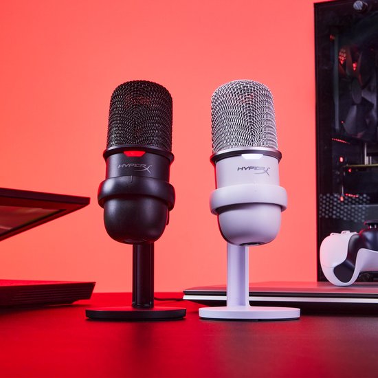 Zwarte en witte HyperX microfoons met standaard, naast een computerkast en gamecontroller.