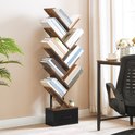Een boekenkast in boomvorm staat in een woonkamer, gevuld met boeken, naast een raam met gordijnen en een plant.