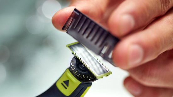 Hand houdt een zwarte kam op de felgroene scheerkop van een OneBlade scheerapparaat.