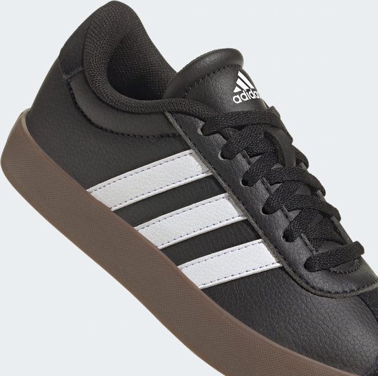 Zwarte sneaker met witte Adidas-strepen op de zijkant en een bruine zool. Logo op de tong.