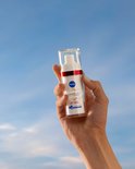 Hand houdt Nivea Cellular Luminous630 Anti-Age & Anti-Spot serum vast tegen een blauwe hemel.