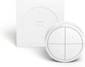 Een witte Philips Hue Tap Dial Switch met zijn witte houder. De ronde schakelaar heeft vier knoppen, elk met twee kleine puntjes.
