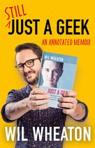 Wil Wheaton tient un livre intitulé 'Still Just a Geek'. Il porte une chemise violette et des lunettes.