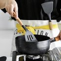 Spatule grise avec fentes dans une poêle grill noire. Une personne porte un tablier.