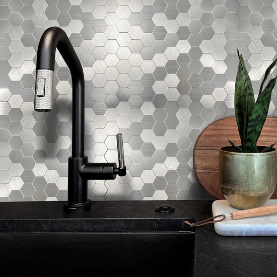 Zilverkleurige hexagon tegels met geborstelde afwerking, op een keukenachterwand met zwarte kraan en gootsteen.