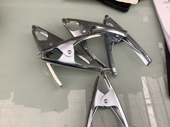 Vier metalen zeilklemmen, zilverkleurig, op een glanzende tafel.