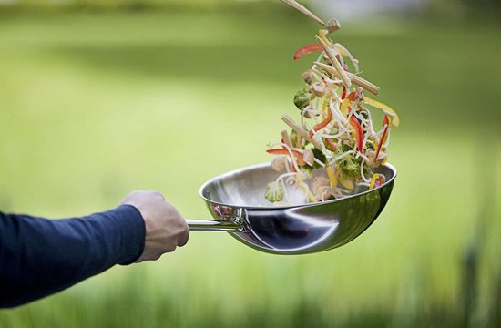 Hand houdt zilverkleurige RVS wokpan met koksingrediënten die eruit vallen.