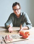Een man met bril zit aan tafel met spek, witte bonen en tomaten.