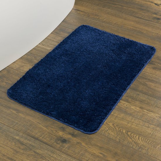 Een donkerblauwe, shaggy badmat ligt op een houten vloer naast een witte badkuip.