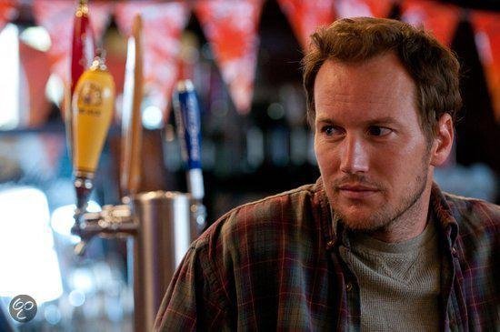 Man met bruin haar in geruit overhemd, in een bar met bierkranen.