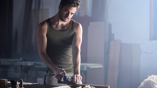 Man in tanktop schaaft hout met een schaafmachine in een werkplaats.