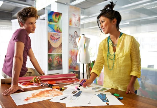 Een man en een vrouw in een creatieve studio bekijken ontwerpen op papier. Zij houdt een gele Stabilo Boss markeerstift vast.