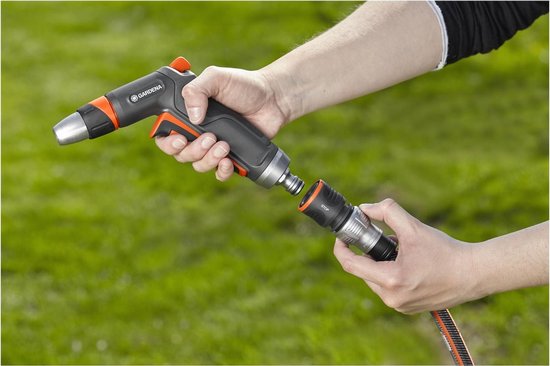 GARDENA waterstop slangkoppeling met oranje accenten, vastgehouden in handen met groene grasachtergrond.