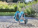 Een blauwe tuinslanghaspel met grijze slang en oranje handvat, staat op een geplaveid terras in een tuin.